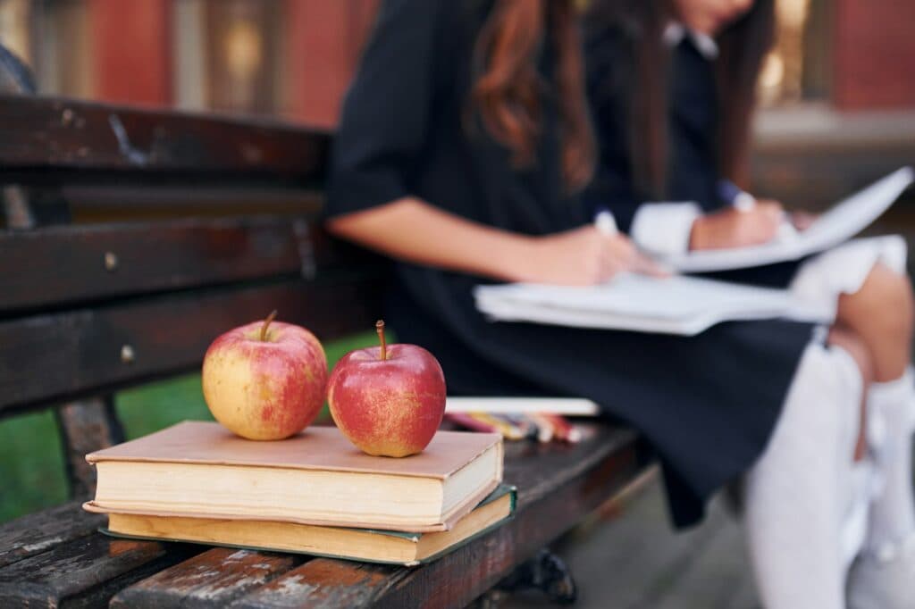 Apples is on the book. Two schoolgirls is outside together near school building