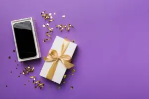 Opened gift box with gold ribbon and smartphone on color background, top view