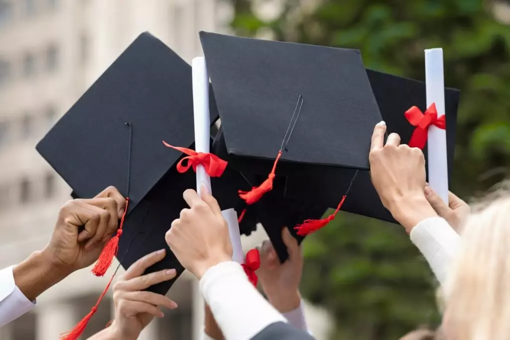 Graduation hats and diplomas in students hands, closeup